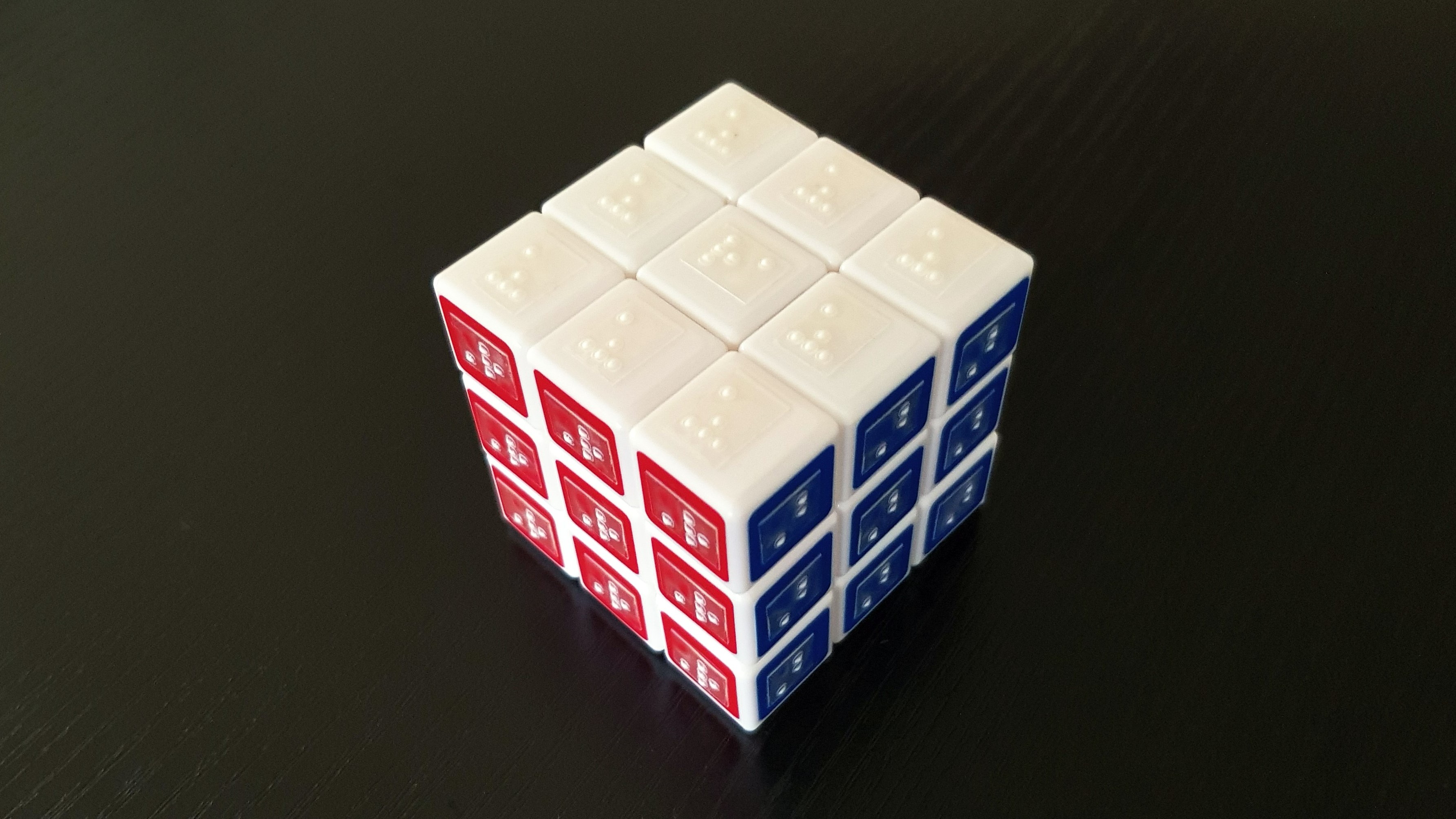 A colourful puzzle cube with braille labels on each small square.