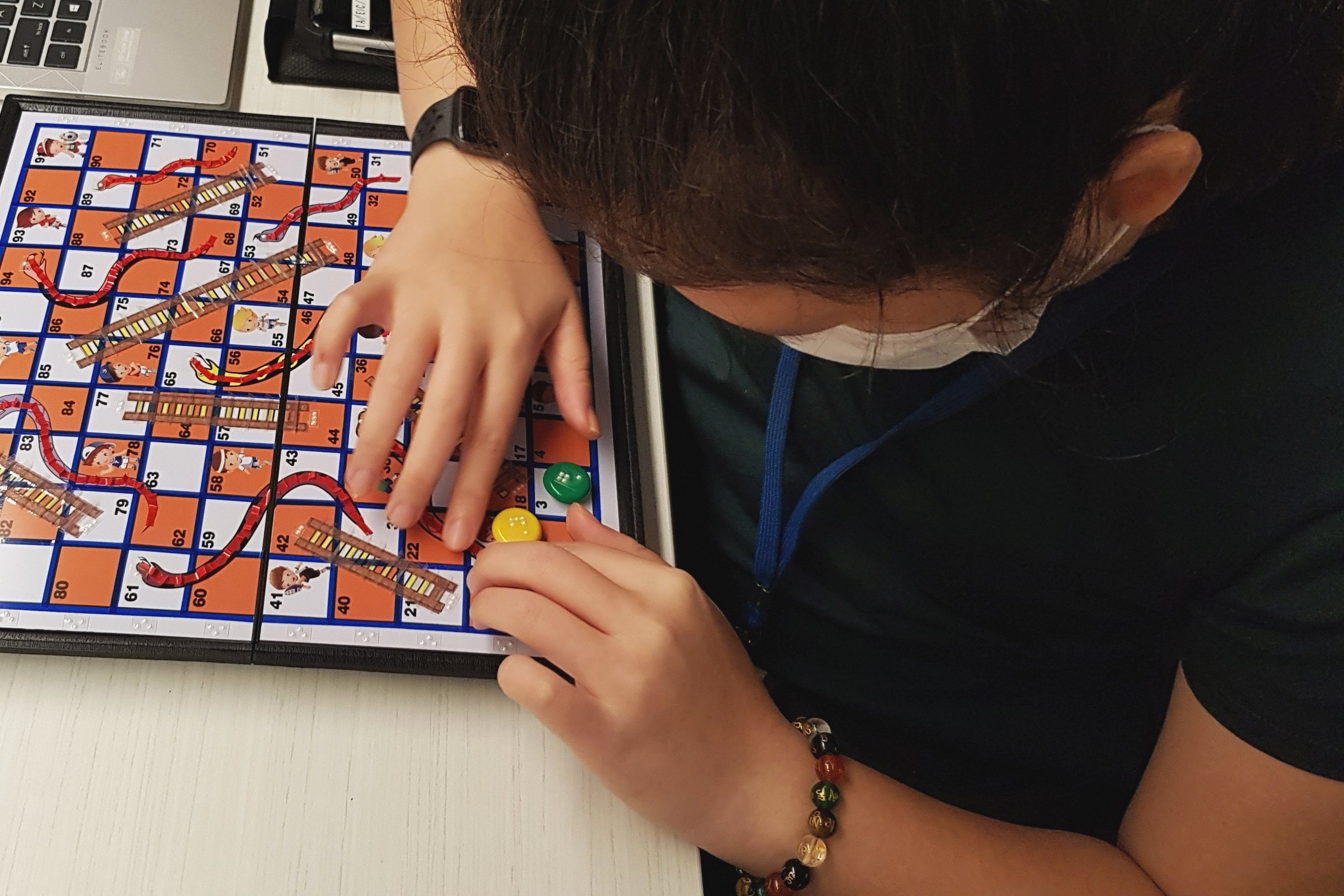 Photo of Siew Ling touching the board of the Snakes and Ladders game, which has been made accessible with tactile images for the ladders and snakes printed on the board.