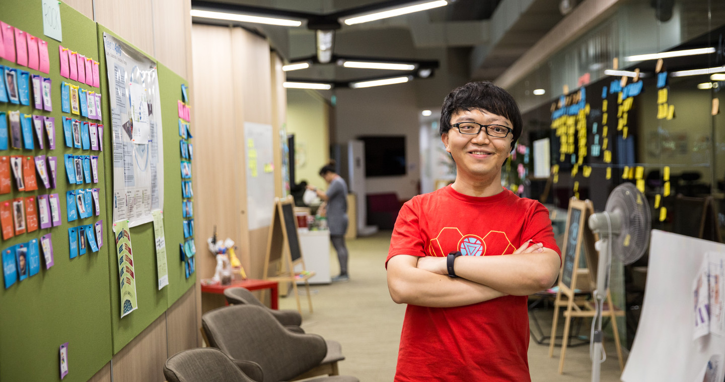 A young man smiling with his arms folded in an office