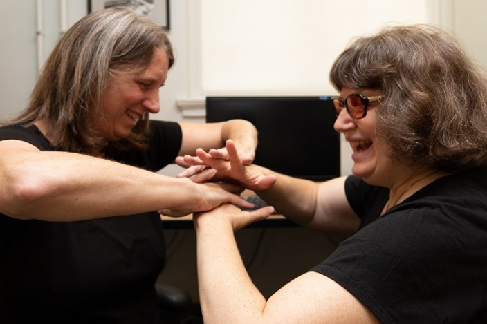 A deafblind lady and her interpreter using their palms to make the sign for the Protactile American Sign Language movement together.