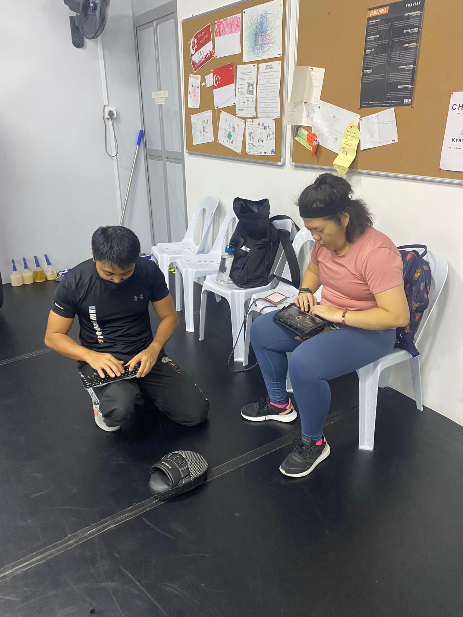Siew Ling’s trainer is typing while kneeling on the floor, while Siew Ling sits beside him on a chair to read what he shares