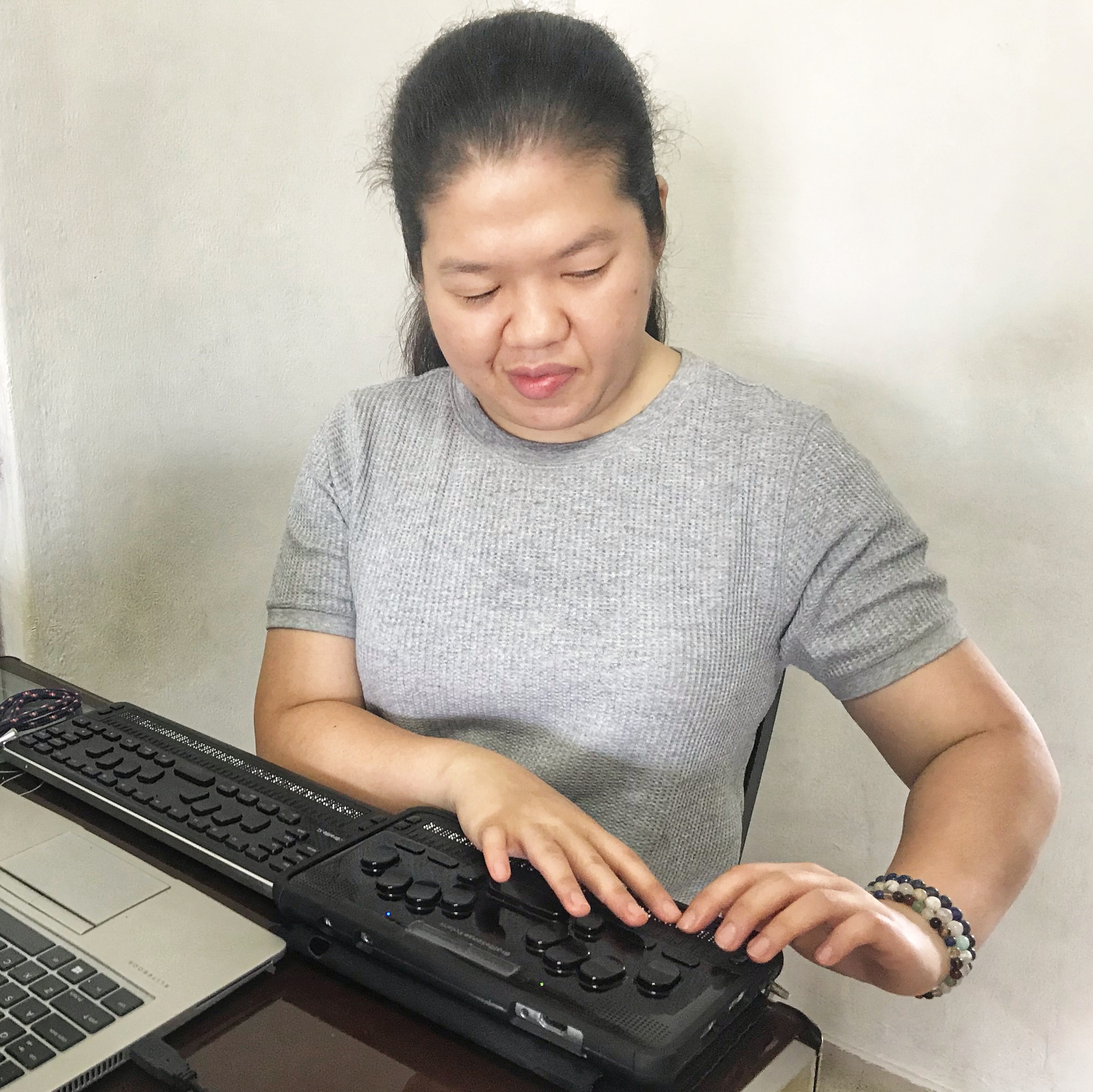 A picture of Siew Ling reading with the use of BrailleSense Polaris and BrailleSense QBraille