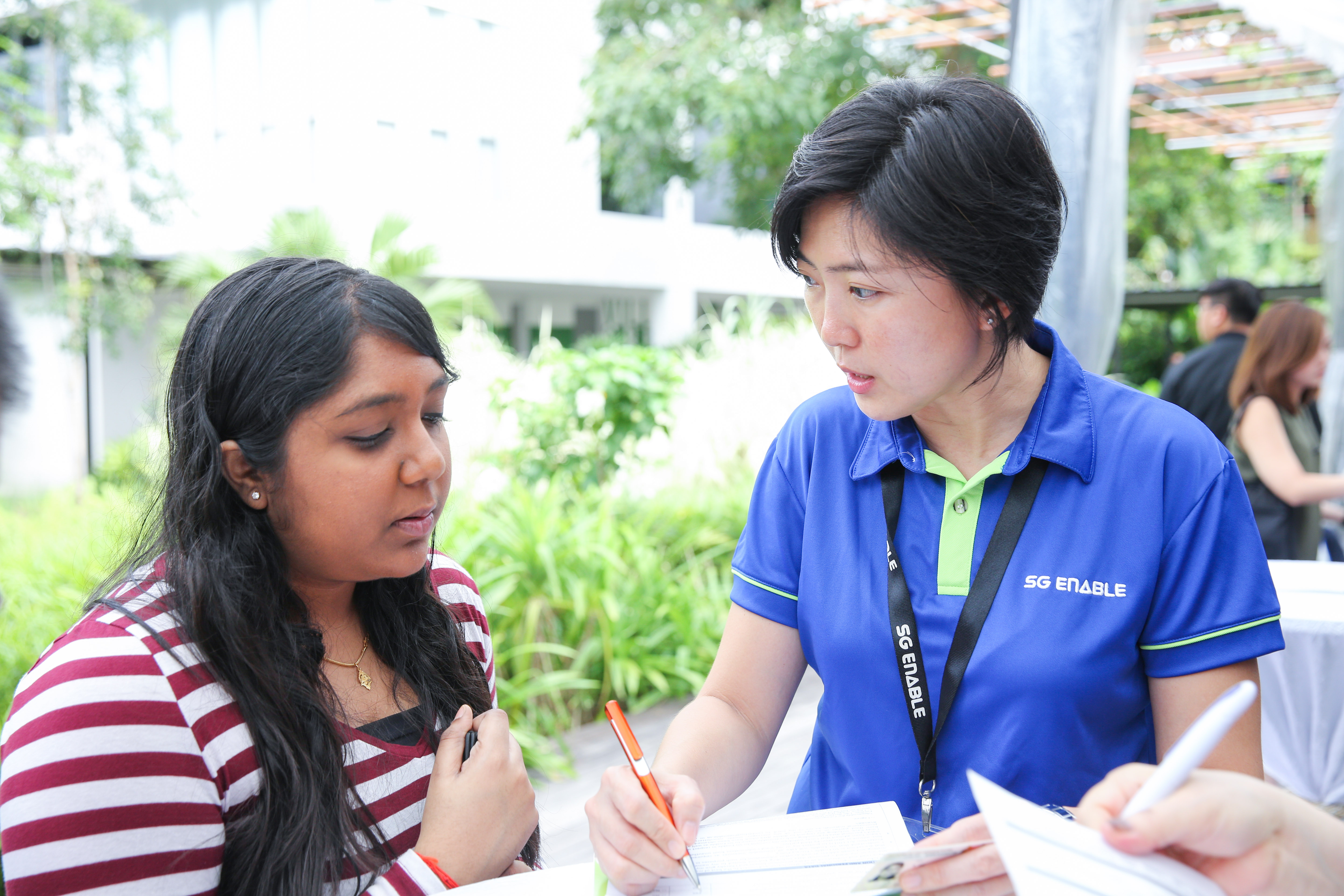 Lady in blue SG Enable t-shirt talking to lady with red and white striped blouse at the Enabling Village