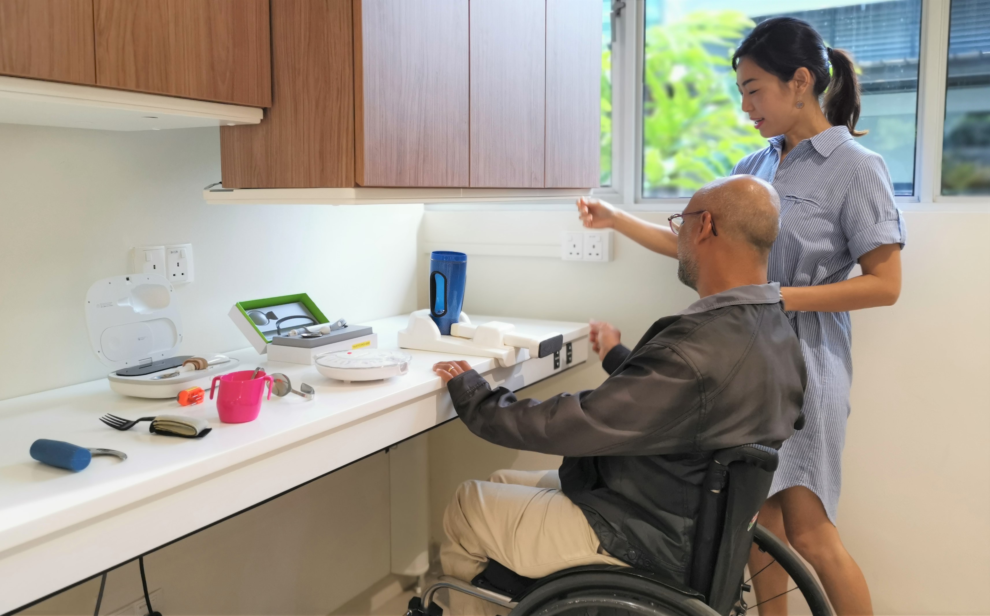 A male wheelchair user trying out a height-adjusted table with the help of a female companion.