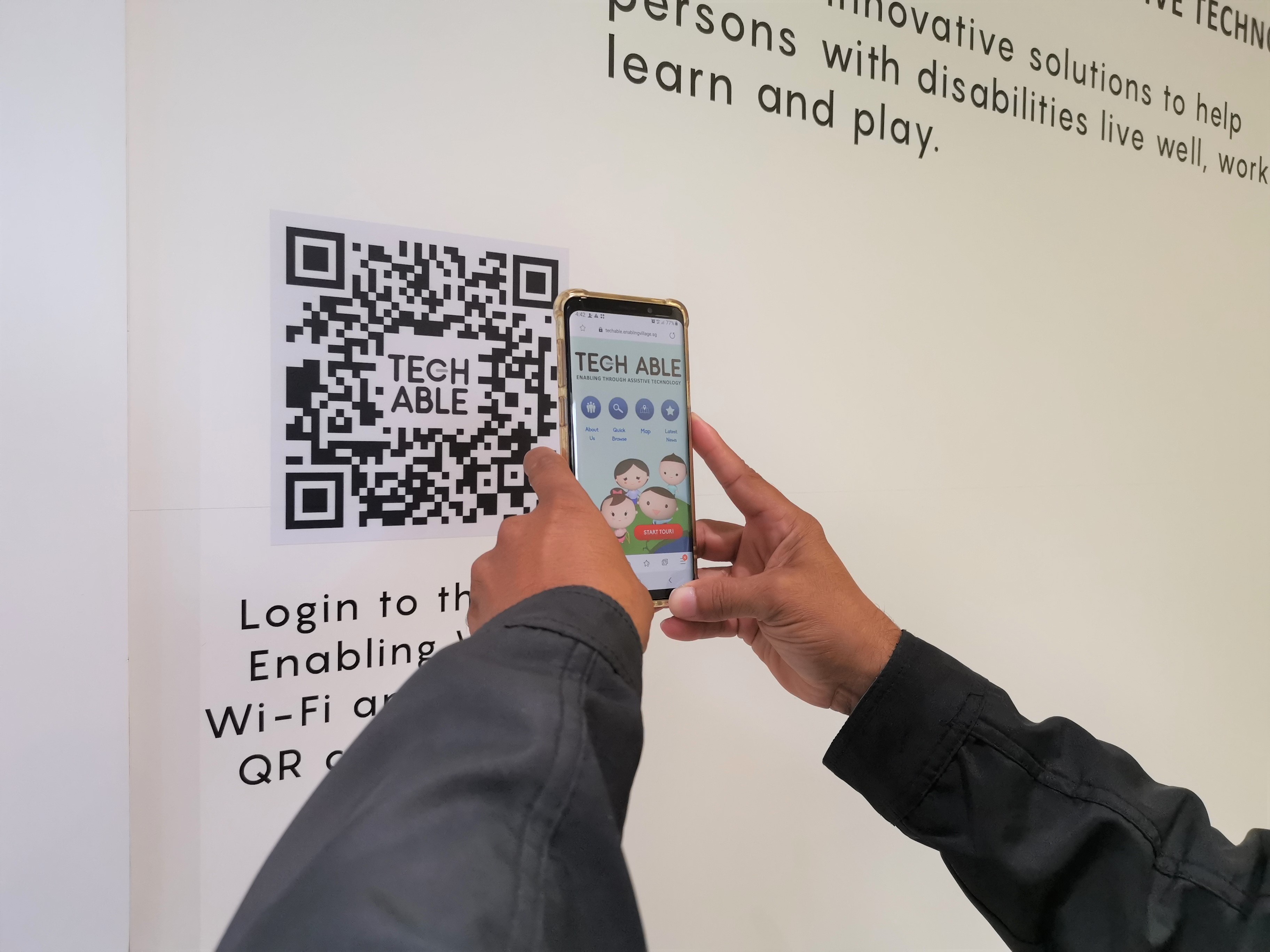 A visitor scans the QR code on the wall to launch the interactive web app which contains information about the assistive technology devices on display.