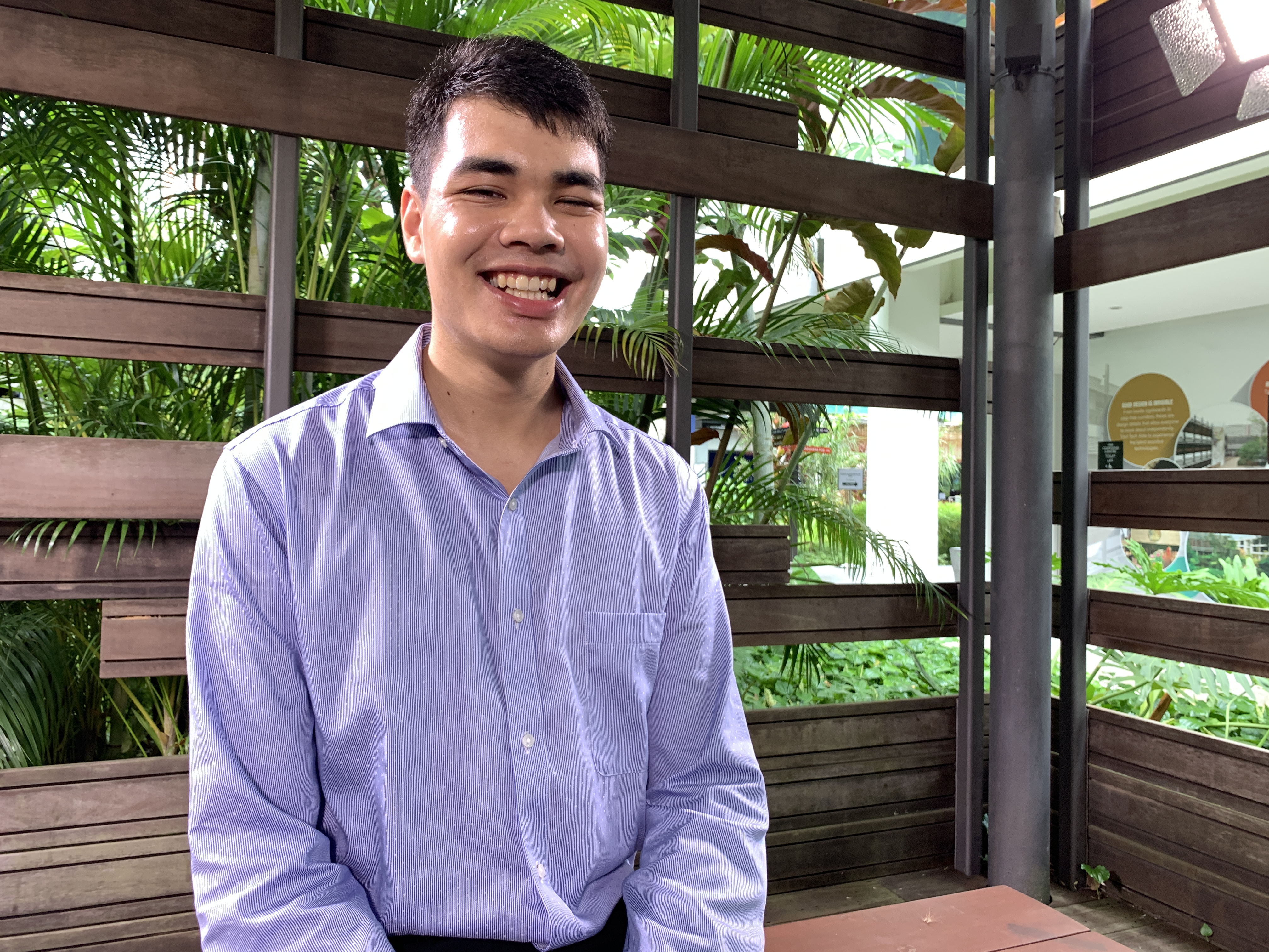 Smiling boy sitting on a wooden bench in an enclosed wooden cabana at the Enabling Village.