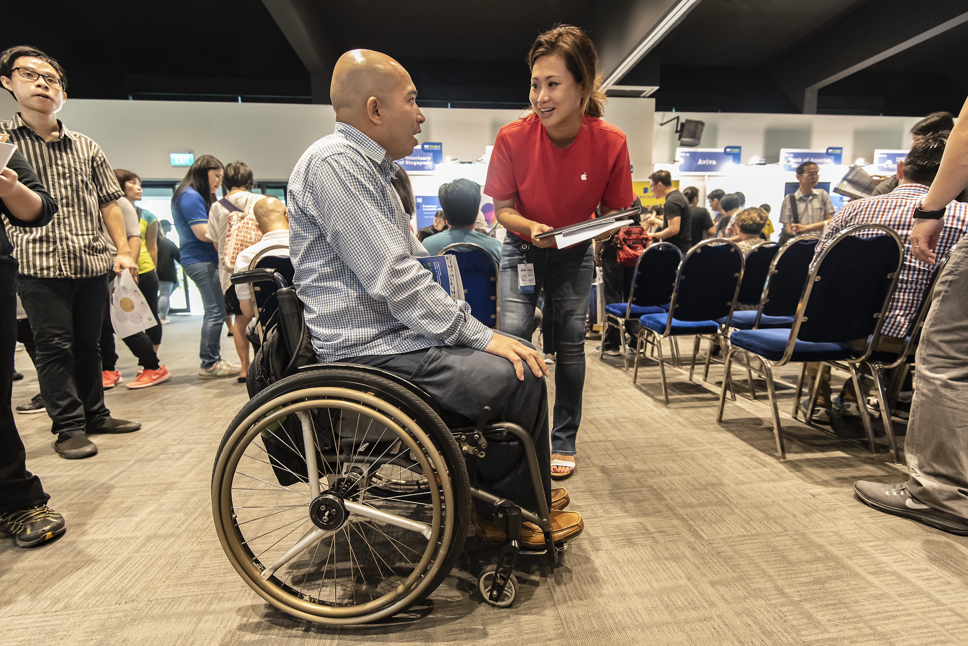 Lady with red blouse and jeans talking to man on wheelchair at a training and career fair.