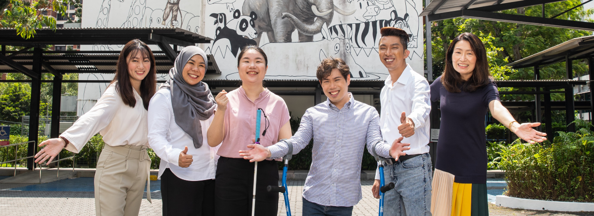 Five cheerful individuals, including persons with disabilities, are posing with their hands held wide open and giving thumb-ups.