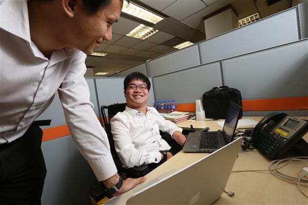 An intern with disability conversing with his colleague at his desk.